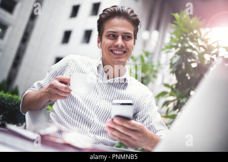 Happy handsome businessman looking at computer screen while typing something on laptop keyboard during work break outdoors, businessman with headphone Stock Photo