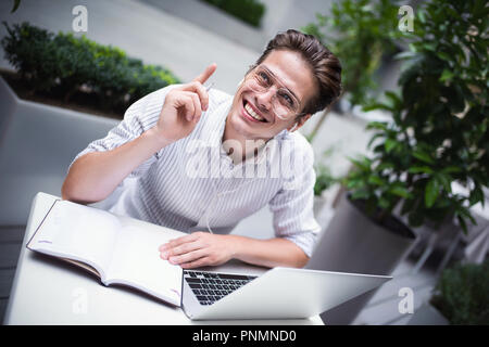 Happy handsome businessman mixes his break and job outdoors, businessman with headphones write some new ideas in notebook sitting in cafe. Stock Photo