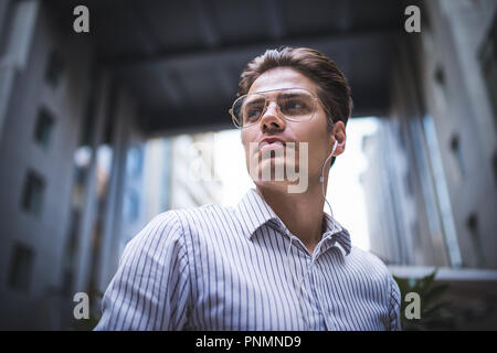 Happy handsome businessman at street with headphones looking through shoulder. Stock Photo