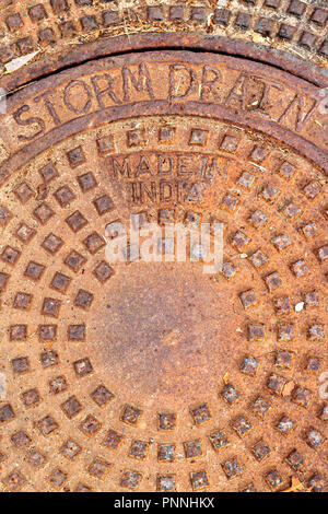Round circular pattern of squares, rust orange storm drain cover, words storm drain and Made in India, an industrial mandala Stock Photo