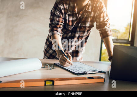 Man working, engineering checking, writing on blueprint and looking on laptop at site construction work. Stock Photo