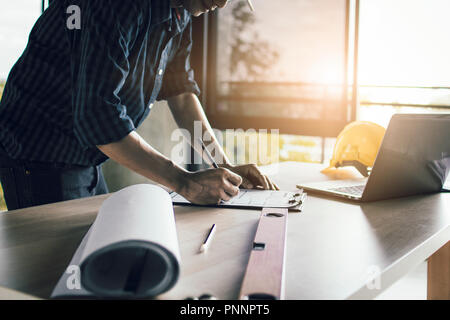 Man working, engineering checking, writing on blueprint and looking on laptop at site construction work. Stock Photo