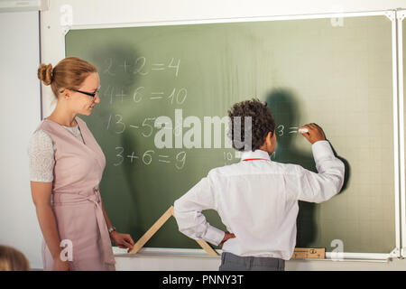 boy solving addition and subtraction on board. schoolboy writing solution of mathematical operation Stock Photo
