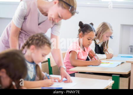 Teacher helping kids with their homework in classroom at school Stock Photo