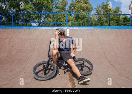 Rider sitting on BMX in skate park resting after riding Stock Photo