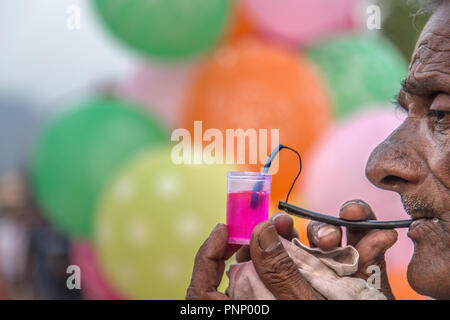 Old Indian street vendor blows soap bubbles to attract customers as he sells bottles of bubble solution Stock Photo