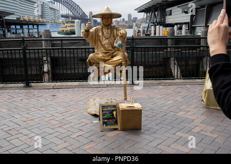 23 March 2018 : Circular Quay, Sydney, Australia: Street performer in gold paint elevating off the floor with his legs crossed Stock Photo