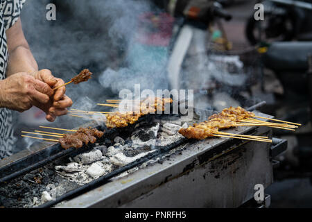 Hawker grilling satay on top of charcoal fire in George Town, Penang. A tourist attraction in Malaysia for it’s popular street food and heritage. Stock Photo