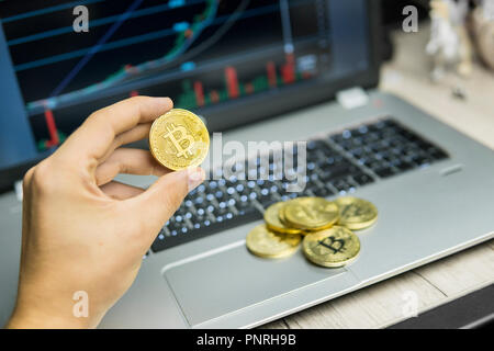 Male businessman hand holding bitcoin on a background of growth graph on a screen of laptop and . Virtual money Financial growth concept on chart background. Trading Mining. Stock Photo