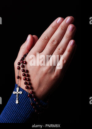 Female hands praying holding a beads rosary with Jesus Christ in the cross or Crucifix on black background. Woman with Christian Catholic religious fa Stock Photo