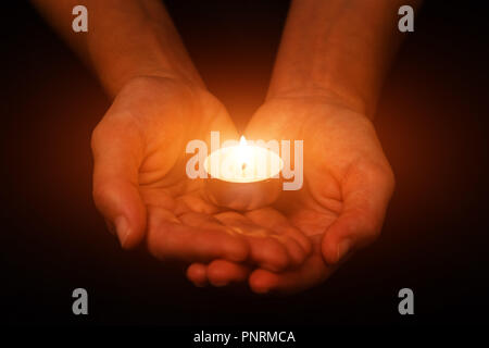 Hands holding and protecting glowing lit or burning candle candlelight on darkness. Black background. Concept for prayer, praying, hope, vigil, night  Stock Photo