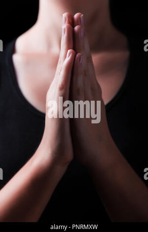 Low key, close up of hands of a faithful woman praying, with hands folded and palms together in worship to god, on a black background. Concept for rel Stock Photo