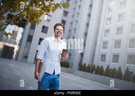 Cheerful young handsome well dressed man holding laptop computer and cup of coffee. Stock Photo