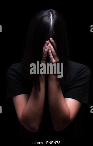 Emotional woman crying and covering the face with the hands hiding the tears, on a black or dark background. Concept for victim depression pain grief Stock Photo