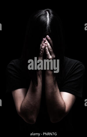 Emotional woman crying and covering the face with the hands hiding the tears, on a black or dark background. Concept for victim depression pain grief Stock Photo