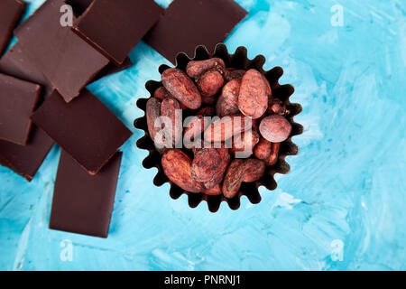 Cocoa beans background on blue table. Dark chocolate pieces and crushed cocoa powder carob. Top view. Copy space. Stock Photo