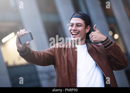 Selfie mania! Excited young guy is making selfie on a camera. He is wearing casual trendy wear and snap back Stock Photo