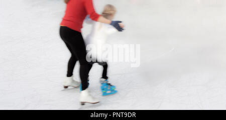 Belgrade, Serbia - January 8, 2018: Little girl learning to ice skate holding hands with the instructor mother, smooth motion blur from behind Stock Photo
