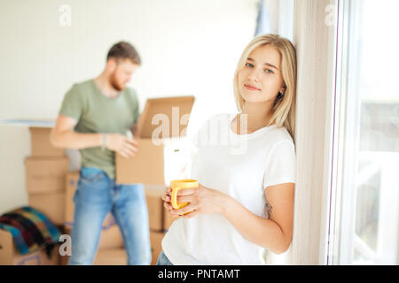 woman posing at camera while her boyfriend or husband unpacks boxes. couple moving into their new home Stock Photo