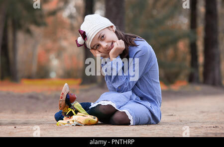 girl sitting on the floor of a park with her hands on her face next to a rag doll Stock Photo
