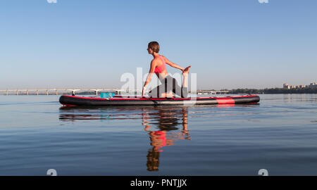 Woman doing yoga on sup board with paddle Stock Photo