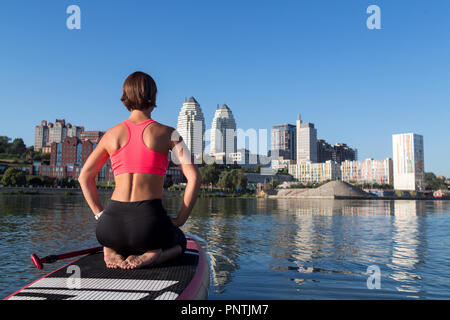 Woman practicing sitting variation of yoga pose on paddle board Stock Photo