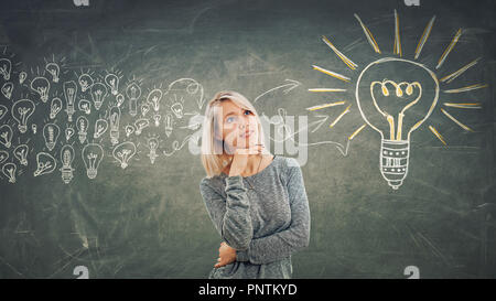 Business concept as a pensive girl with hand under chin, thinking gathering ideas into a big light bulb. Stock Photo