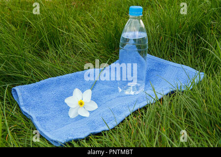 Bottle of mineral water,blue towel and white and yellow color daffodil on green grass Stock Photo