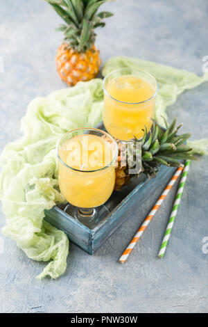 Cocktail with pineapple in two glass glasses with ice and two mini pineapples on a gray background Stock Photo