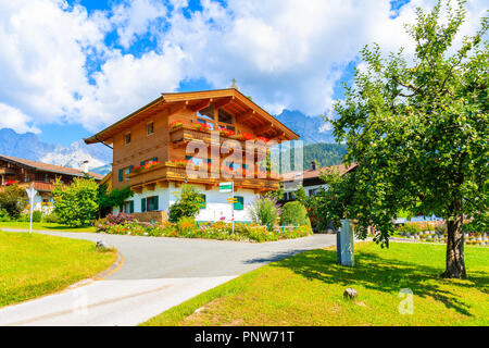Typical wooden alpine house decorated with flowers on green meadow in Going am Wilden Kaiser mountain village on sunny summer day, Tyrol, Austria Stock Photo