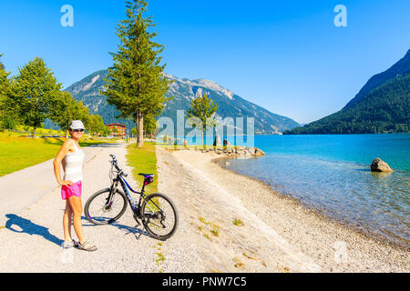 ACHENSEE LAKE, AUSTRIA - JUL 31, 2018: Young woman cyclist standing in Pertisau town on shore of lake which is largest and deepest in Tyrol Stock Photo