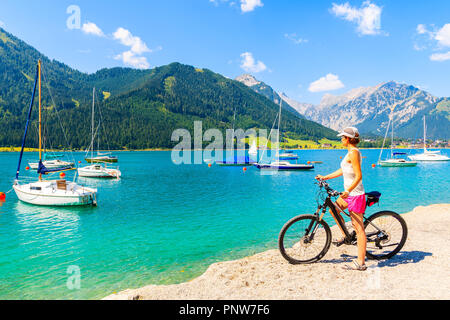 ACHENSEE LAKE, AUSTRIA - JUL 31, 2018: Young woman cyclist on beautiful Achensee lake beach on sunny summer day, Tirol. This lake is most famous lake  Stock Photo