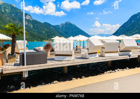 ACHENSEE LAKE, AUSTRIA - JUL 31, 2018: Wicker beach chairs on pier at Achensee lake on sunny summer day, Tirol. During summer this place is very popul Stock Photo