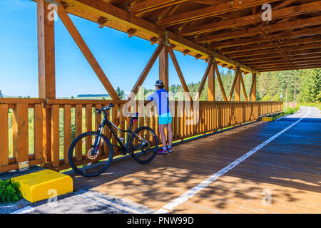 TATRA MOUNTAINS, SLOVAKIA - SEP 12, 2018: Young woman with bike standing on cycling bridge in Tatra Mountains near Trstena village, Slovakia. Stock Photo