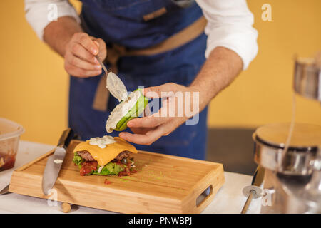 Cook preparing burger adding the sauce on green bun. Stock Photo