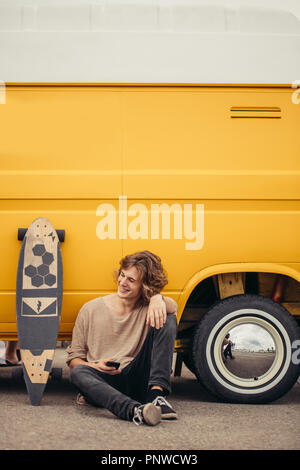 hipster man sitting on longboard using his phone Stock Photo