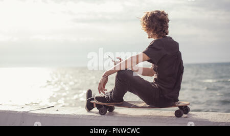 hipster man sitting on longboard using his phone Stock Photo
