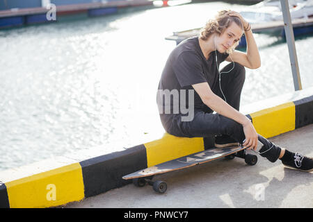 hipster man sitting on longboard using his phone Stock Photo