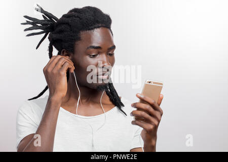 African man wearing headphones and holding his smartphone against white background Stock Photo