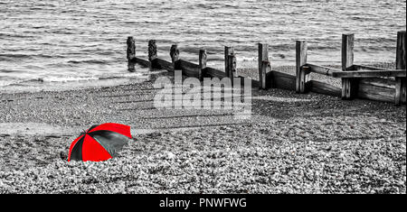 Beach holiday sheltering under an umbrella from a cold wind Stock Photo