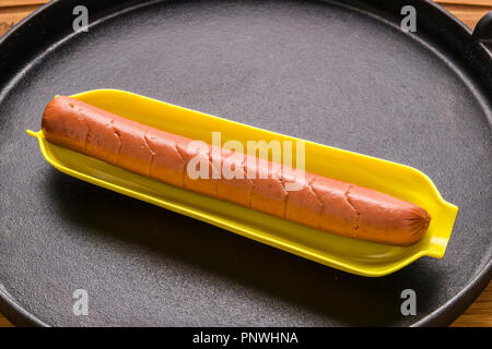 raw hotdog in corn holder in cast iron skillet pan on wood cutting board Stock Photo
