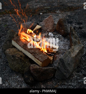 bonfire burning on a rocky shore at dusk with rocks arranged in a circle Stock Photo