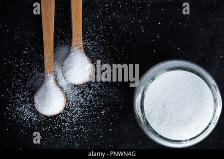 sugar in wooden spoons and glass jar on black background Stock Photo