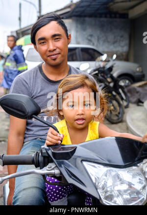 Man and daughter sit on a motorbike at a market in Bali, Indonesia Stock Photo