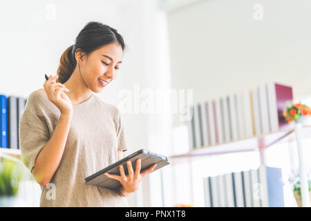 Young beautiful Asian girl working at home office using digital tablet, with copy space. Business owner entrepreneur, small business startup company