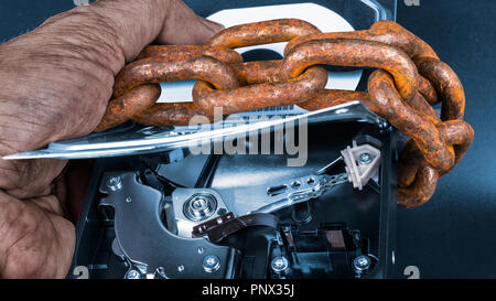 Open hard disk drive. Artistic close-up  EU GDPR data protection. Abstract detail of dirty hand holding data storage device locked by old rusty chain. Stock Photo