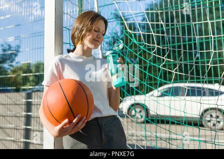 Teenager girl playing basketball with ball on the basketball court drinking water, Stock Photo