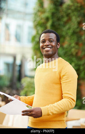 Successful and confident young businessman in yellow pullover looking at you while working outdoors Stock Photo