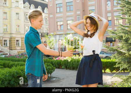 Teenager boy congratulates the girl with bouquet of flowers outdoors. Friendship and people concept Stock Photo