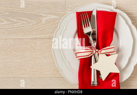 Festive Christmas table setting place setting with white china plates, red cloth napkin and silverware on rustic wood background. Horizontal with empt Stock Photo